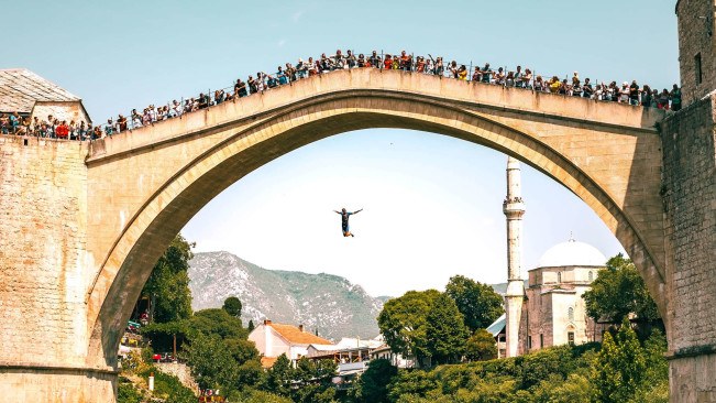 A man diving of the old bridge in Mostar with a crowd of people watching