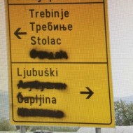 A road sign in Bosnia with the cyrillic text intentionally blacked out by graffiti